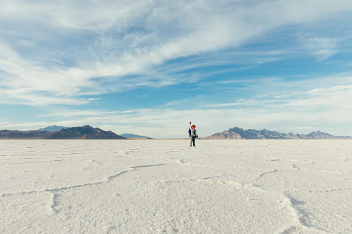 A young boy businessman is dressed up as a superhero with cape raises his arm to the sky ready to fly while on the Bonneville Salt Flats in Utah, USA. This young entrepreneur is ready to take on challenges and lead his business into profitability.