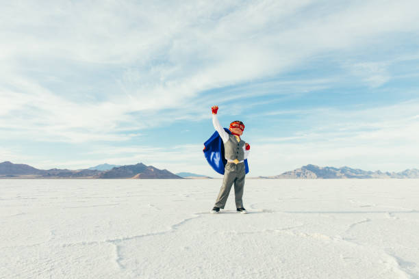 Superhero Business Kid with Arm Raised A young boy businessman is dressed up as a superhero with cape and mask raises his arm in victory while on the Bonneville Salt Flats in Utah, USA. This young entrepreneur is ready to take on challenges and lead his business into profitability. bonneville salt flats stock pictures, royalty-free photos & images