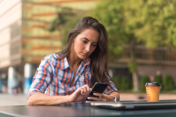 istock Attractive young woman reading a text message on her cell phone. Girl sitting outdoors using smartphone 1150354200