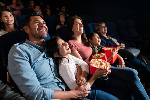 Happy Latin American family watching a comedy film at the cinema and laughing - entertainment concepts