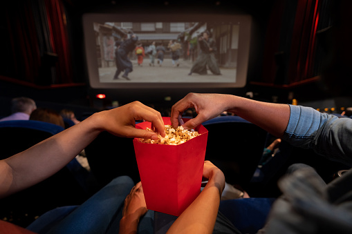 Close-up on a couple at the movies eating popcorn - entertainment concepts. **IMAGE ON SCREEN IS OURS**