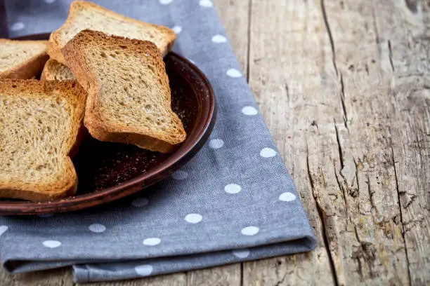 Toasted cereal bread slices on brown ceramic plate closeup on linen napkin on rustic wooden table background. Healthy food for breakfast with copy space.