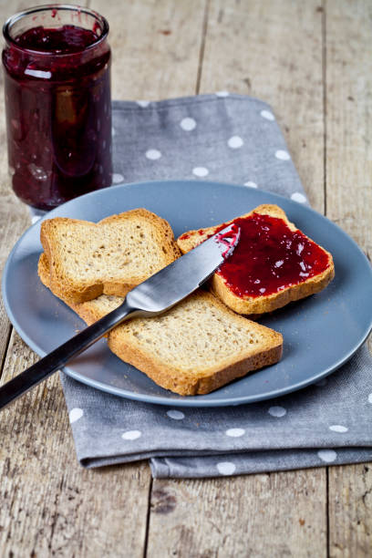 Toasted cereal bread slices on grey plate and jar with homemade cherry jam closeup on linen napkin on rustic wooden table background. stock photo