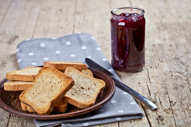 Toasted cereal bread slices on grey plate and jar with homemade cherry jam closeup on linen napkin on rustic wooden table background. stock photo
