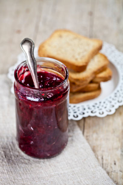 istock Homemade cherry jam in glassjar and fresh toasted cereal bread slices stack on white  plate closeup on linen napkin on rustic wooden table background. 1150355186