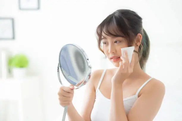 Photo of Beautiful portrait young asian woman smile and joy with skin care use oil blotting paper on face looking mirror in the room, beauty asia girl happy and cheer makeup and cosmetic, health care on facial concept.