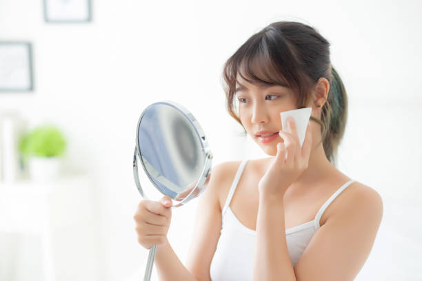 sorriso e alegria asiáticos novos do retrato bonito da mulher com o óleo do uso do cuidado de pele que blotting o papel na cara que olha o espelho no quarto, beleza da menina de ásia feliz e elogio da composição e do cosmético, cuidados médicos no c - 2527 - fotografias e filmes do acervo