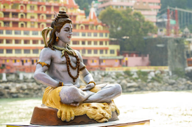 ガンジス川の川岸にシヴァ神に座るの像の見事な眺め。背景にはぼやけた trimbakeshwar 寺。リシケシ、ウッタラーカンド、インド。 - shiva posture ストックフォトと画像