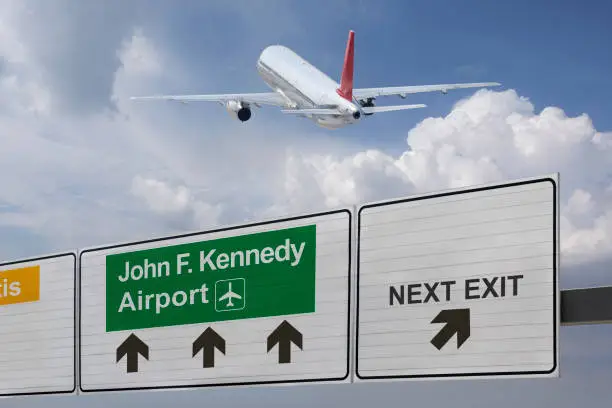 Photo of Road sign indicating the direction of John F. Kennedy airport and a plane that just got up.