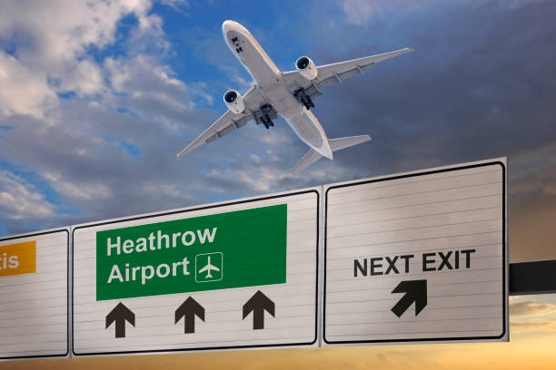 Road sign indicating the direction of Heathrow airport and a plane that just got up. stock photo