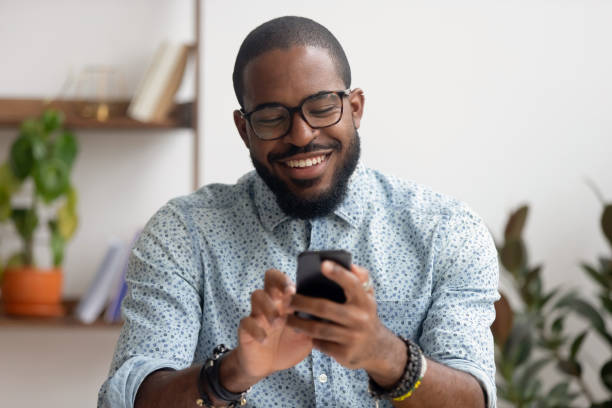 職場で携帯電話のモバイルアプリを使用して幸せなアフリカ系アメリカ人のビジネスマン - portable player ストックフォトと画像