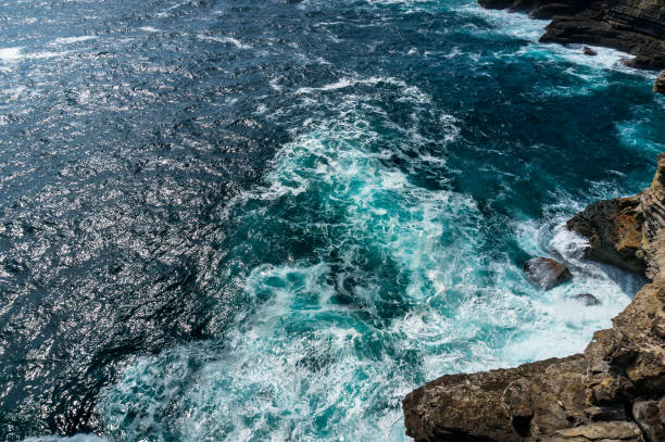 Elevated, birds eye view of ocean water surface with tough waves and cliff rocks. Nature texture background