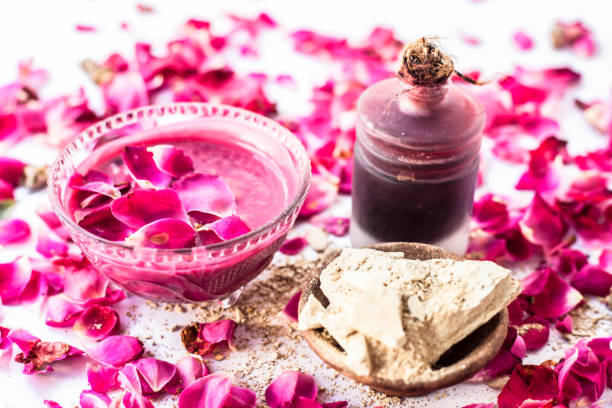 Rose water face pack isolated with rose petals well mixed with mulpani mitti or fuller's earth in a glass bowl and entire ingredients present on the surface,Used  For Exfoliation. stock photo