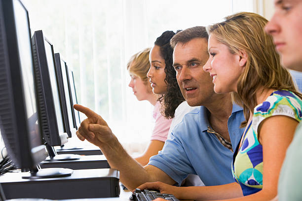 istock Male teacher assisting college student in a computer lab 115039380