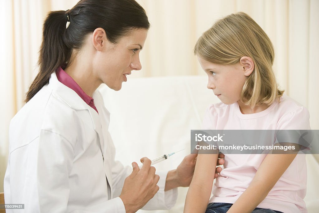 A doctor giving a young girl a shot in an exam room Doctor giving needle to young girl in exam room in doctors surgery Child Stock Photo