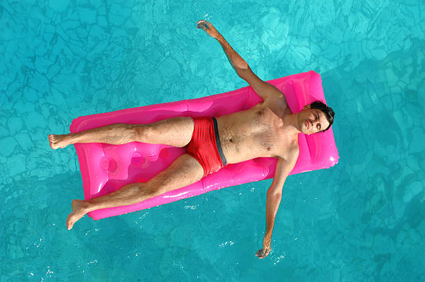 istock Young man floating on a mattress in water pool 115039827