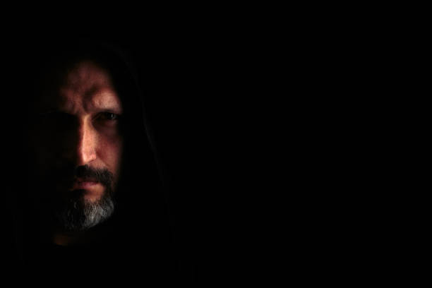 istock Brutal man with a gray beard in the hood with sharp shadows on a black background. Copy space. 1150402816