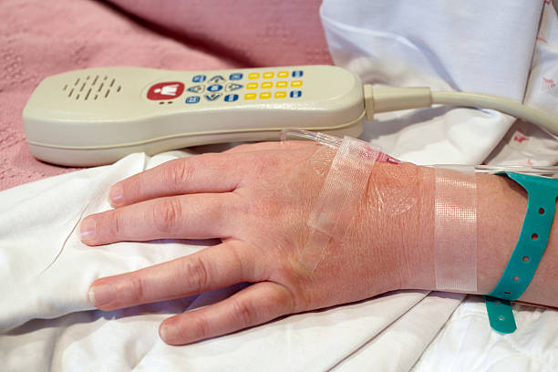 Female Hospital Patient's Hand, IV Drip, and TV Remote Control stock photo