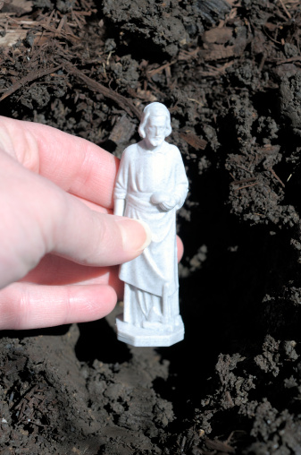 A St. Joseph figurine being buried in the ground by a female hand. This is a ritual performed in real estate by the home seller to bring good luck with selling a house.