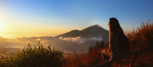 Image of a young female traveler on top of the Mt Batur volcano in Bali, Indonesia, taken in the early morning, just after sunrise. She is wearing casual clothes, enjoying the beautiful view from the top of the mountain.
