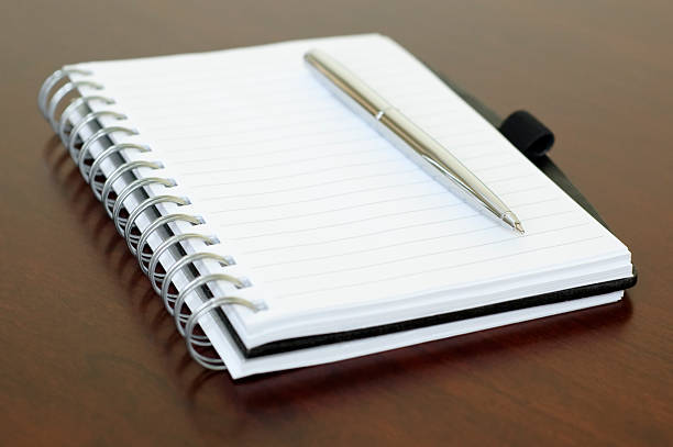 istock Spiral Notebook and Chrome Pen on Brown Wooden Office Desk 115040649