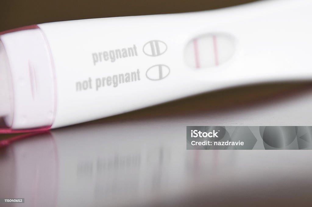 Positive Pregnancy Test Close-Up on a Brown Wooden Table A pregnancy test closeup showing "pregnant" with selective focus on a brown table.  Positive Emotion Stock Photo