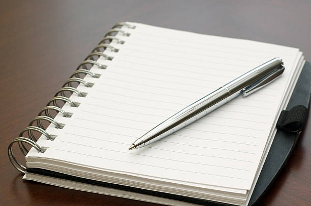 istock Spiral Notebook and Silver Pen on a Brown Desk 115040849