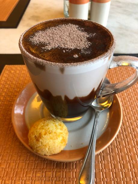 istock Image of hot chocolate mug with cream, dusted icing sugar, cocoa sprinkles and macaroon biscuit cake, cup and saucer on orange table, hot chocolate drink in cafe / coffee shop, afternoon tea for two taking a break 1150416191