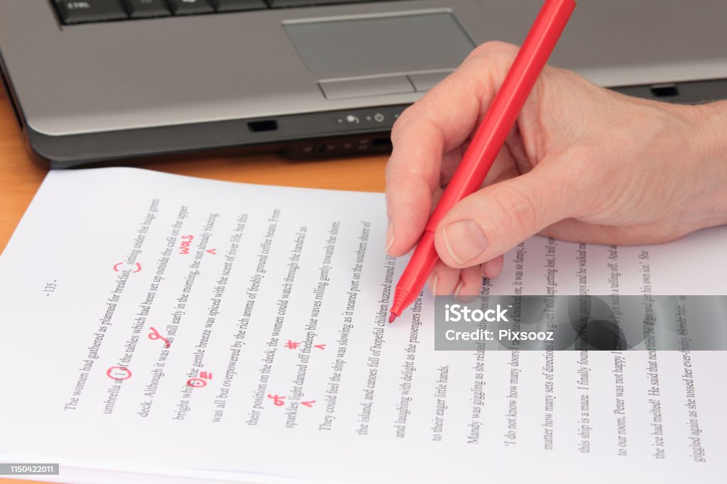 Hand Proofreading a Manuscript beside Laptop A hand proofreading a novel manuscript beside a laptop (manuscript text created by contributor) Editor Stock Photo