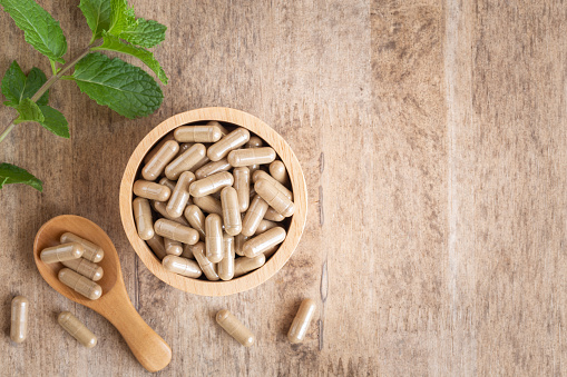 Herbal capsules  in cup on wooden table background . Top view of medicine for healthy and capsules on the spoon wooden
