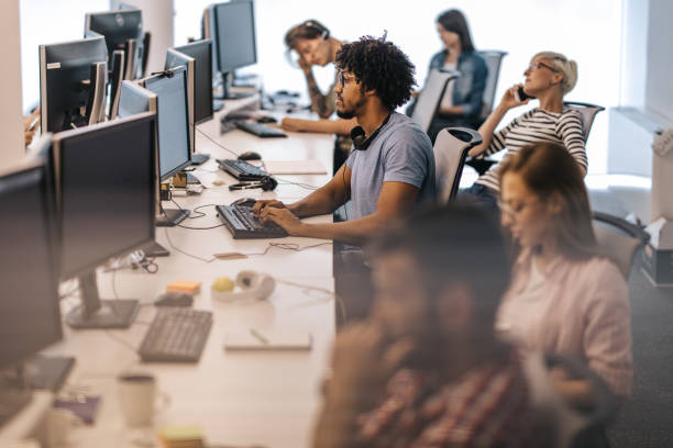 istock African American programmer working on desktop PC in the office full of people. 1150426742