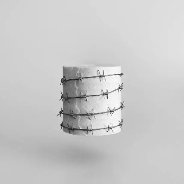 Photo of A roll of toilet paper wrapped in red barbed wire on a gray uniform background.