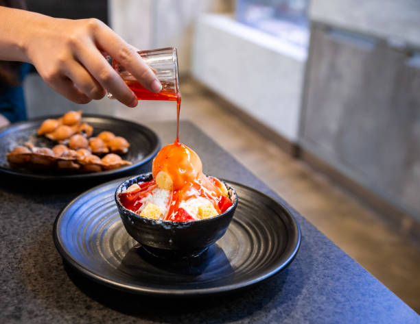 Hand pouring strawberry sauce on Bingsu, a Korean shaved ice dessert with sweet toppings such as vanilla ice cream, cheese cube and sweetened condensed milk. It's very popular dessert. With copy space