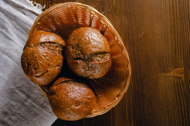 Craft three bread buns in a wicker basket, on a wooden cutting board. Simple breakfast on wooden background. Close-up view. copy space