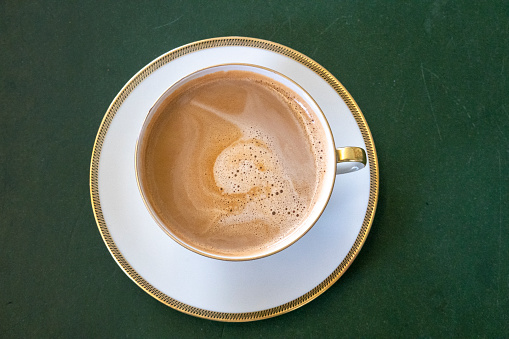 Top view from an old fashioned mug with gold rim and milk coffee on old dark green table