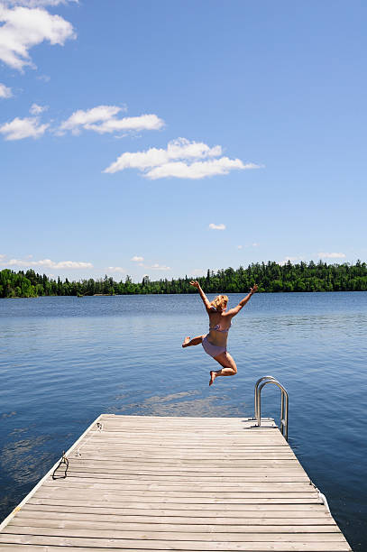 istock Young woman jumps off dock on beautiful summer's day. 115044304