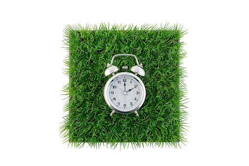 Old style alarm clock on square of green grass field isolated on white background with clipping path