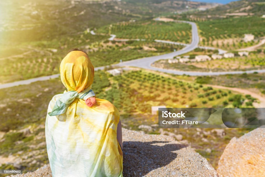 A lonely Muslim woman  traveler in a colorful scarf sits on top of a mountain. Freedom Stock Photo