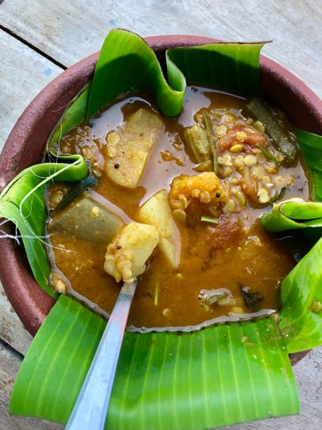 Stock photo of Indian sambar meal food, sambar stew / chowder broth soup with lentils in dish for South Indian savoury breakfast photo served with banana leaf, breakfast recipe in Kerala, South India, served in rustic unglazed clay dish with banana leaf, black peppercorns, green chillies and ornate spoon imagen de comida de sambar indio, estofado de sambar/sopa con lentejas en el plato para el desayuno salado de la india del sur servido con hoja de plátano, receta de desayuno en kerala, sur de la india, servido en plato de arcilla sin esmaltar con hoja de