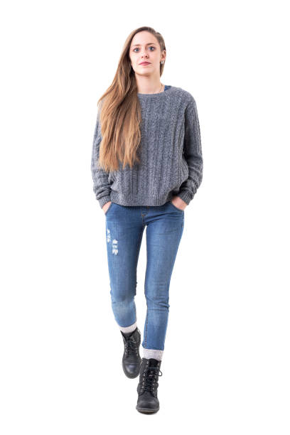 cute young pretty woman in sweater and jeans walking towards camera with hands in pockets. - aproximando imagens e fotografias de stock