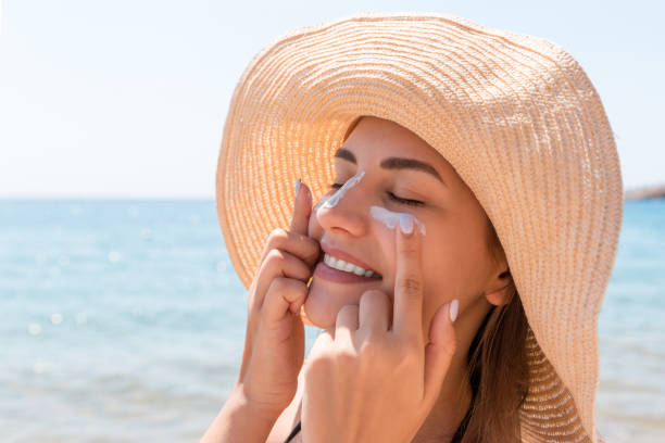 smiling woman in hat is applying sunscreen on her face. indian style - sky human hand water white imagens e fotografias de stock