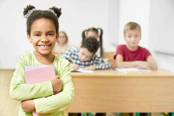 istock Happy schoolchild standing in classroom, holding books. 1150459347