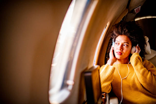istock Urban arfo-american woman sitting on a private jet and looking through a window while listening to music through headphones 1150465236