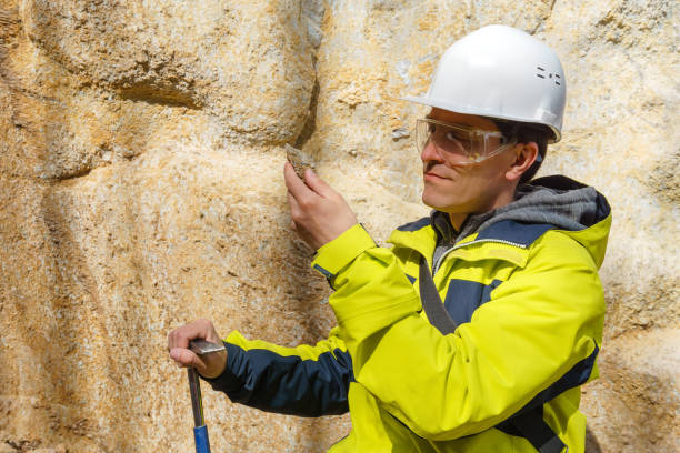 geologist examines a sample of stone outdoor male geologist in helmet and protective glasses examines a sample of the mineral outdoors against a rock geologist stock pictures, royalty-free photos & images