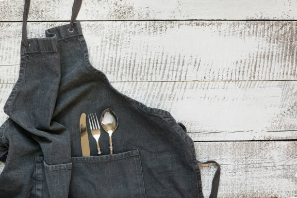 istock Gray kitchen apron with silverware on wooden table. View from above with space for text. 1150469722