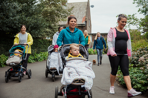 A group of mothers are walking together with their children on a fitness bootcamp.