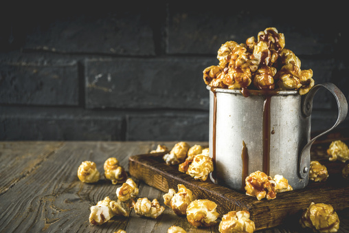 Homemade sweet caramel pop corn, with caramel topping, dark rustic background copy space