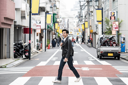 Cool young man in his 20s walking on road in city, smiling, confidence, individuality