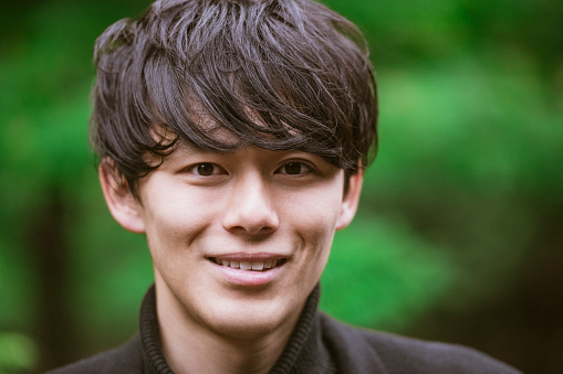 Cheerful young Asian man in his 20s smiling towards camera with defined cheekbones