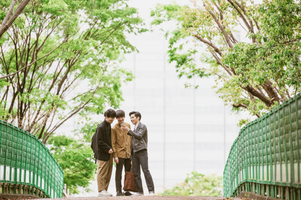 istock Young Japanese man showing two friends mobile phone in park 1150475310